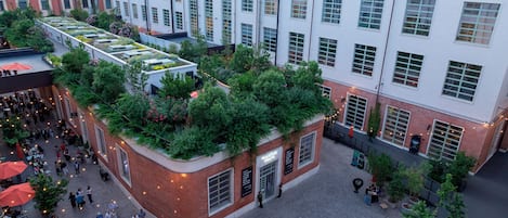 A rooftop garden with greenery and seating areas, surrounded by buildings with large windows and a brick facade.
