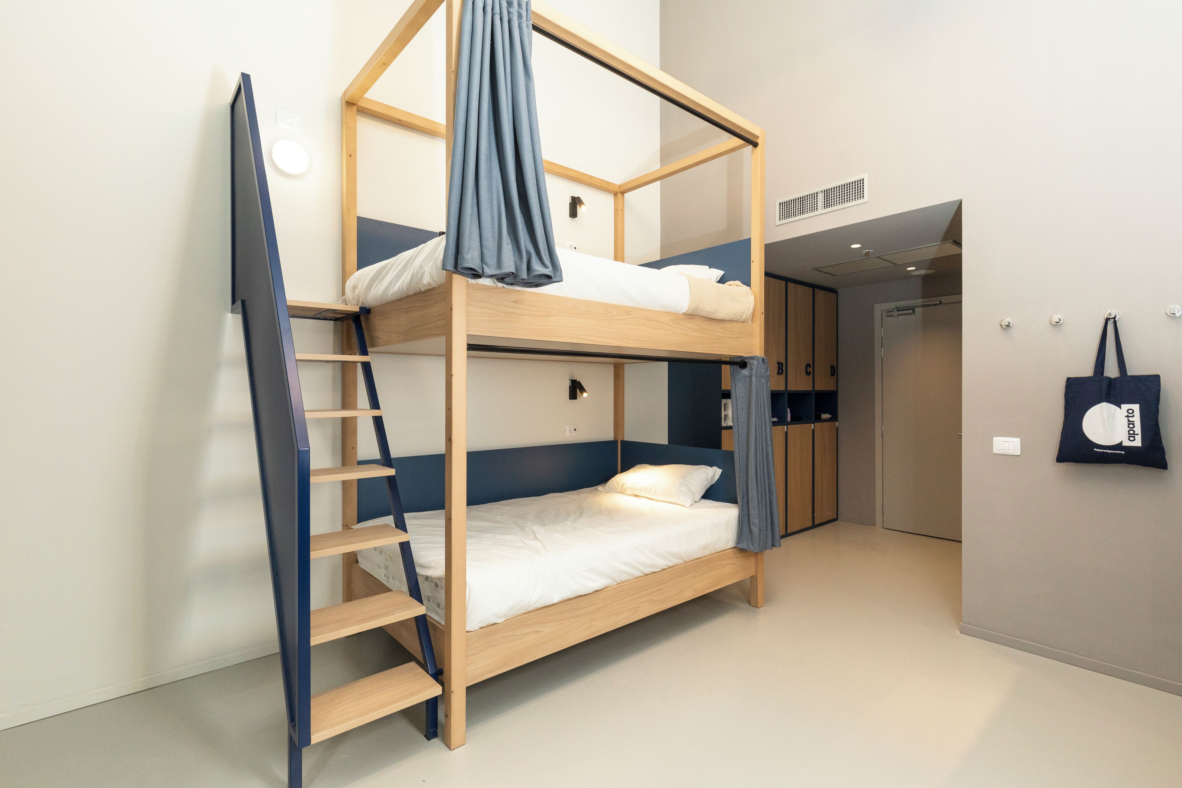 A bunk bed with a ladder, a small desk, and a wall-mounted bag rack in a hotel room.