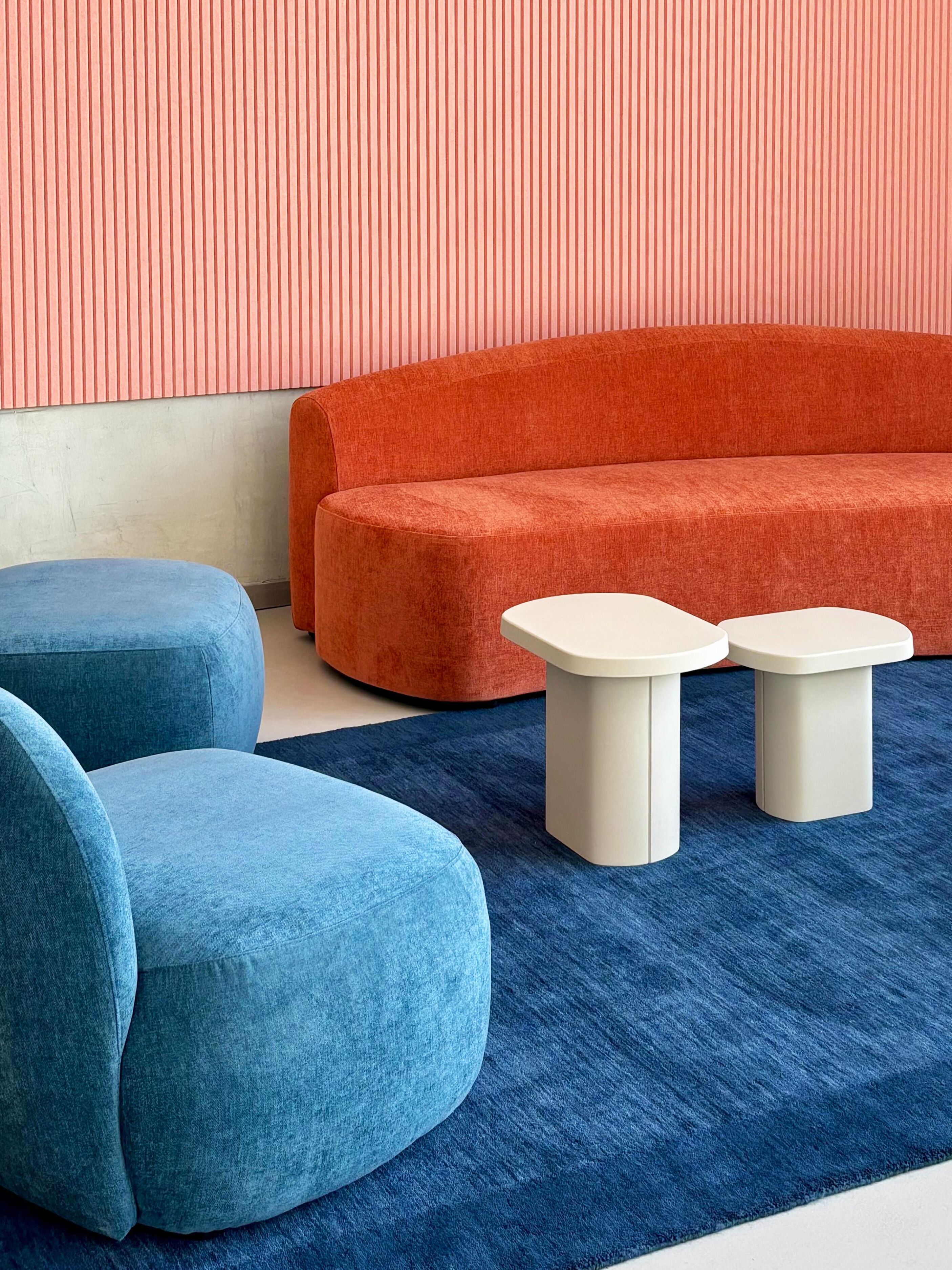 A modern living room with a large orange sofa, two blue armchairs, and two white side tables on a blue carpet.