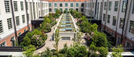 A courtyard with a central garden, surrounded by buildings with large windows and a tiled roof.