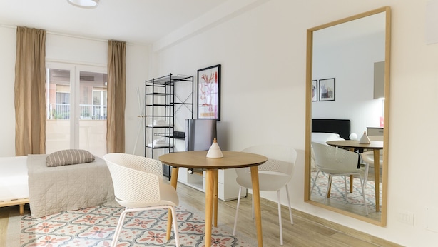 A hotel room with a bed, a round table with chairs, a large mirror, and a window with curtains.