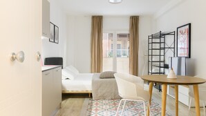 A compact hotel room with a bed, a desk, a chair, a small table, and a window with curtains.