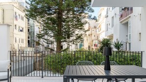 A balcony with a table and chairs, surrounded by a metal fence and a tree.