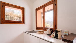 Una cocina con armarios blancos, encimera de madera, una tetera, una cafetera y una ventana con vistas a árboles.