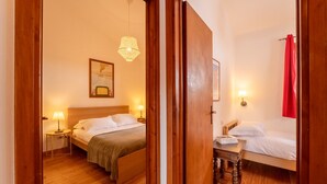Habitación de hotel con dos camas, suelo de madera, una mesita de noche con lámpara, una lámpara colgante y una cortina roja.