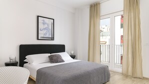 A bedroom with a large bed, a nightstand, a bedside table, a framed picture on the wall, and a view of the outside balcony.