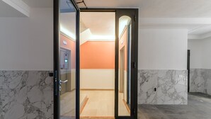 A modern hotel lobby with marble flooring, a glass door entrance, and a view into a brightly lit room with orange walls.