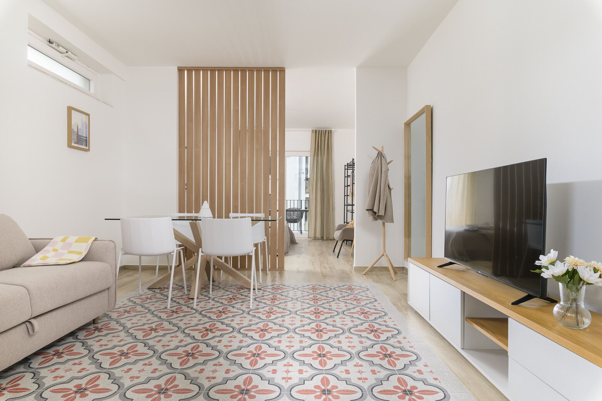 A modern living room with a sofa, dining table, chairs, a TV, and a patterned rug.