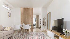A modern living room with a sofa, dining table, chairs, a TV, and a patterned rug.
