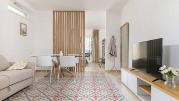 A modern living room with a sofa, dining table, chairs, a TV, and a patterned rug.