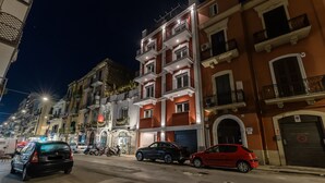 A street view at night with multi-story buildings, parked cars, and streetlights.