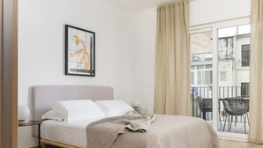 A bedroom with a bed, a nightstand, a framed picture, and a view of an outdoor balcony.