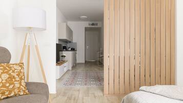 A modern, well-lit room with a sofa, a floor lamp, a bed, and a kitchen area in the background.