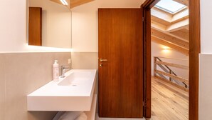 A modern bathroom with a wooden door, a white sink, and a skylight above.