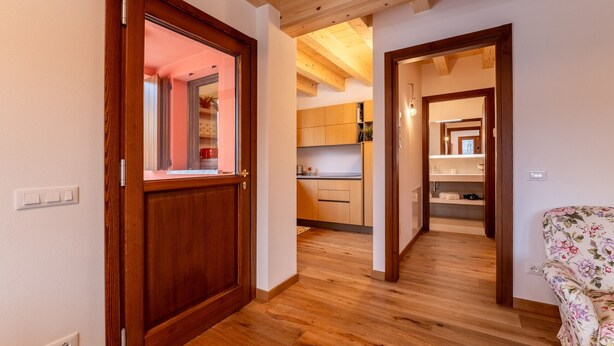 A hallway with wooden flooring and doors leading to a kitchen and a living area.