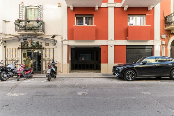 Ein Gebäude mit roter Fassade, ein schwarzes Auto davor sowie zwei Roller am Gehweg.