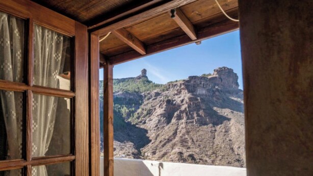 Une pièce avec un plafond en bois et une fenêtre donnant sur un paysage rocheux, avec une falaise.