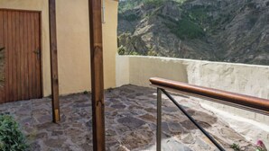 Un balcon dallé de pierres, avec une balustrade en bois, une porte en bois et une vue sur un paysage montagneux.