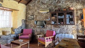 Une pièce rustique aux murs de pierre, avec des poutres apparentes, un lustre et un mobilier traditionnel.