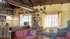 Un intérieur rustique avec un mur en pierre, des meubles en bois, un canapé, une petite table et un coin cuisine équipé d’une cuisinière et d’un évier.