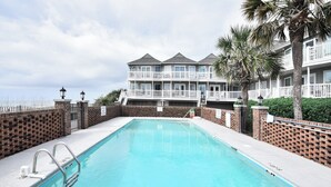 A swimming pool with a brick wall and a building with balconies in the background. - Oceanfront 3 BR Condo with Shared Pool! Admiral's Quarters II 13 (Surfside Beach)