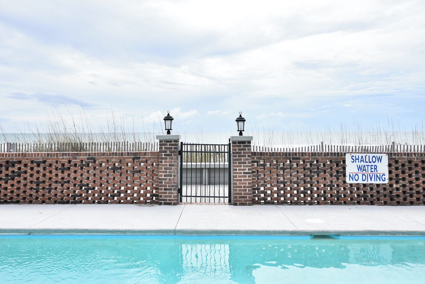A gated swimming pool with a sign indicating shallow water and no diving.