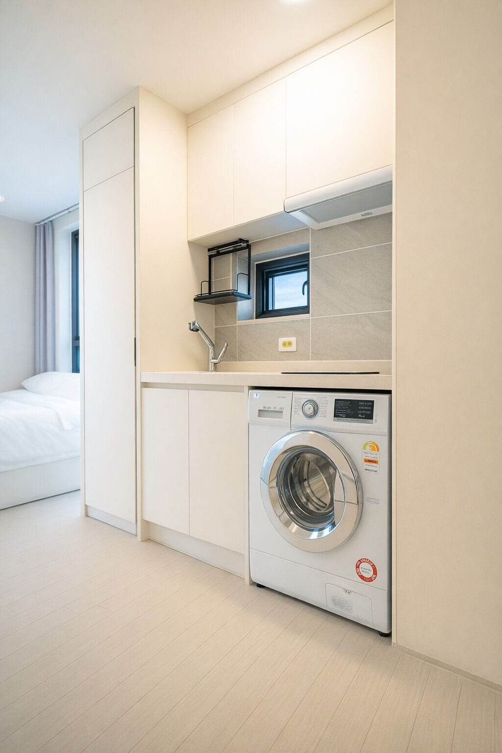Une chambre d’hôtel compacte équipée d’un lave-linge et d’un sèche-linge intégrés, d’une petite fenêtre et d’un lit.