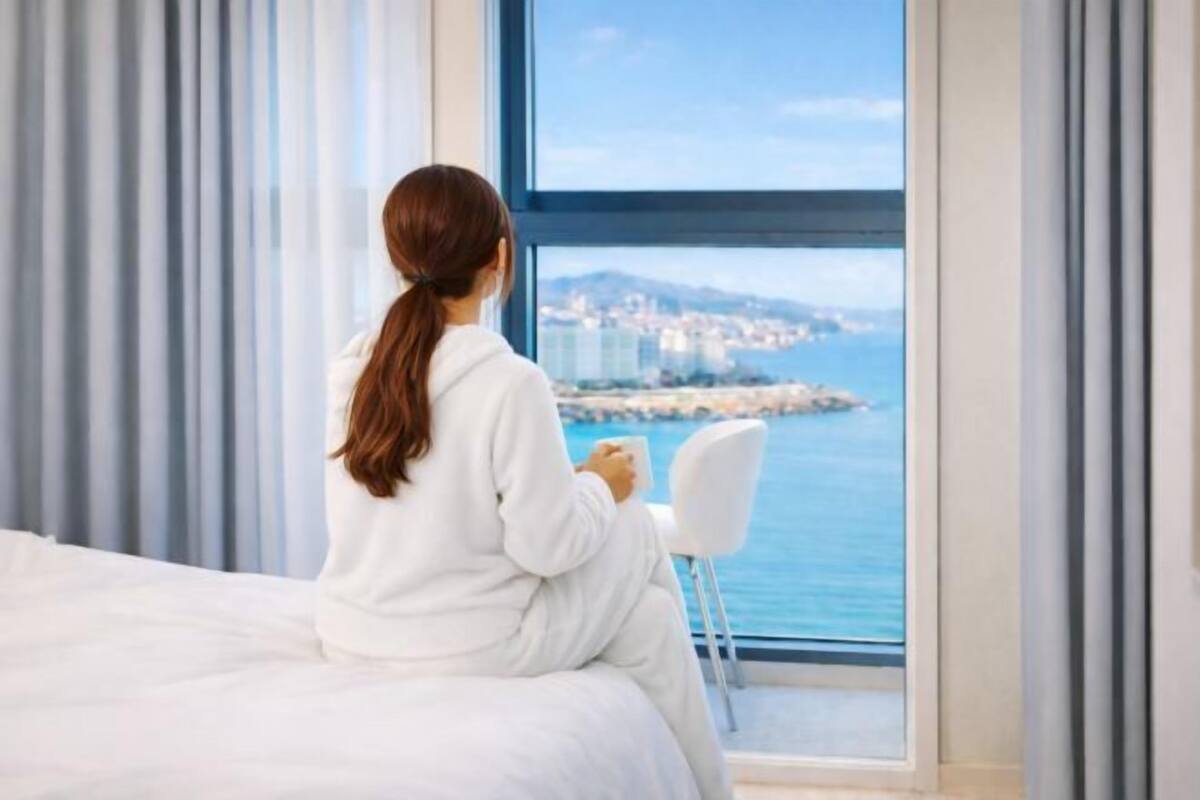 Una persona sentada junto a una ventana con vistas a una ciudad costera.
