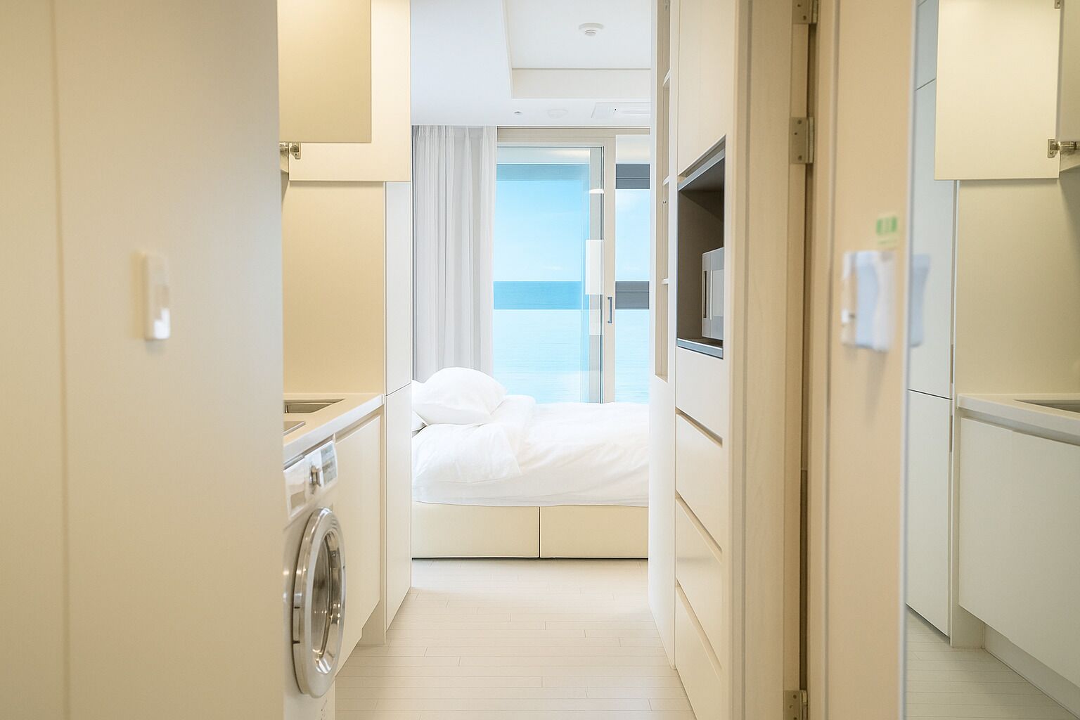A hotel room with a bed, a TV, a washing machine, and a view of the sea.