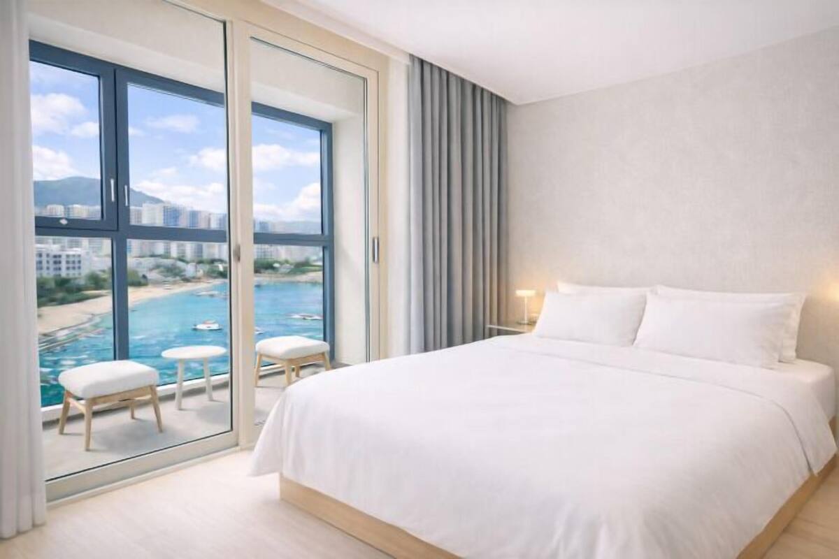 Una habitación de hotel moderna con una cama grande, vista a una playa y piscina, y una puerta corrediza de vidrio.