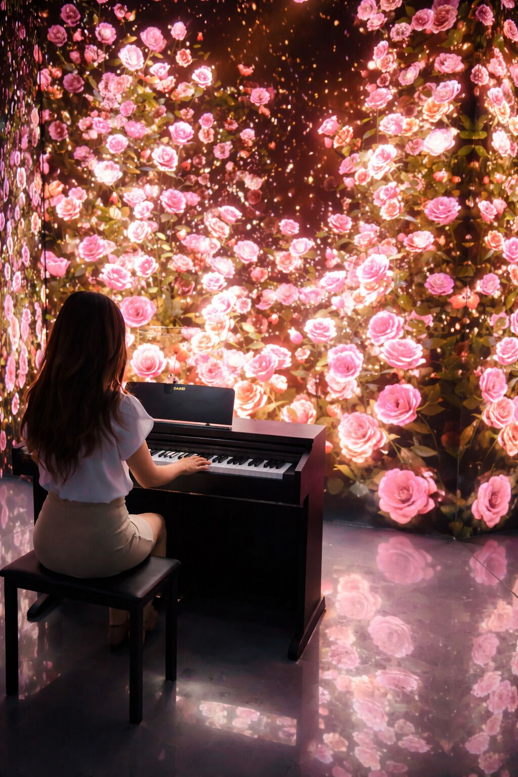 A woman seated at a piano in a room with a floral wall design.