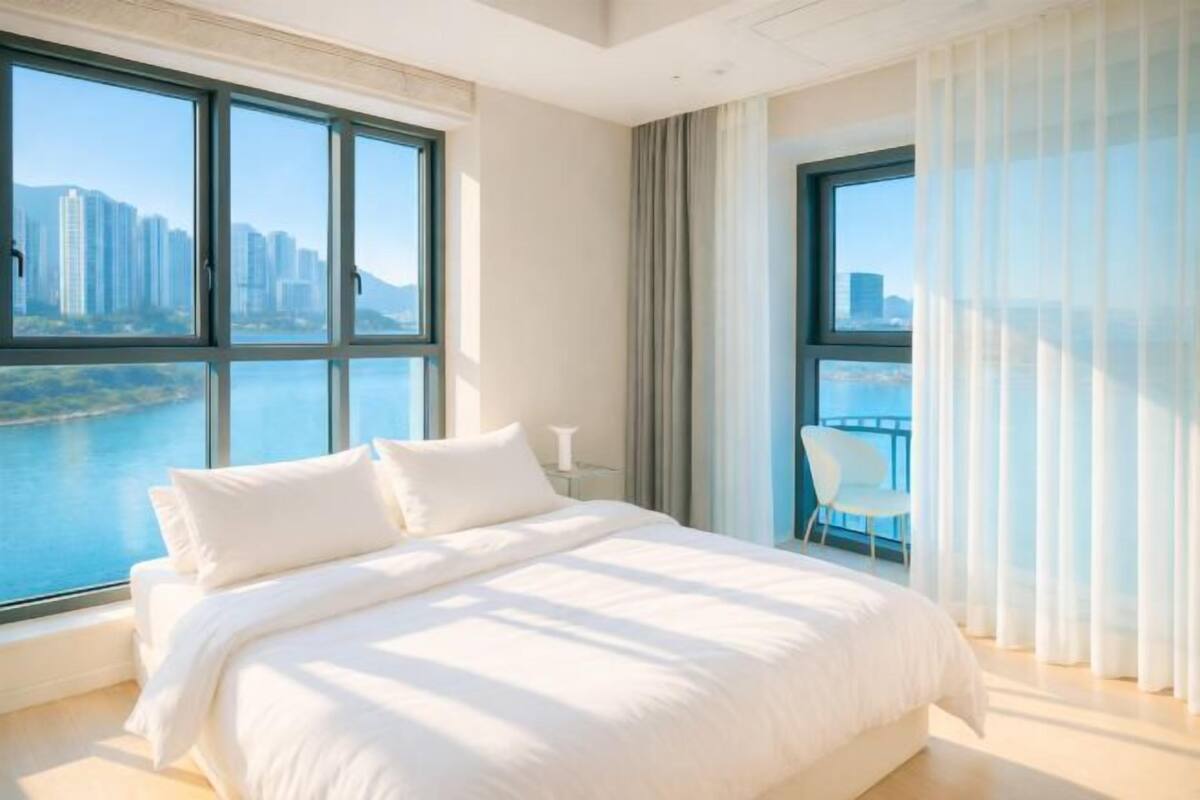 Habitación de hotel moderna con una cama grande, vistas a una masa de agua y un balcón con una silla.