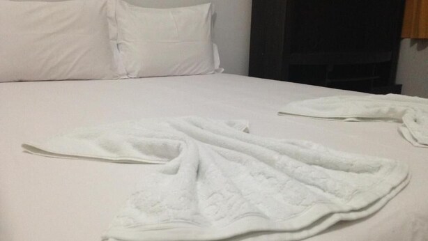 A neatly made bed with white linens and a folded white towel on the bed. - HOTEL COLINAS (Varzea Grande)