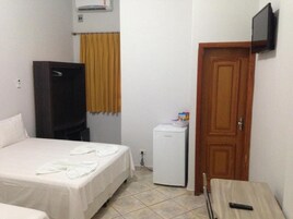 Una habitación de hotel pequeña con cama, televisión montada en la pared, refrigerador y puerta de madera.