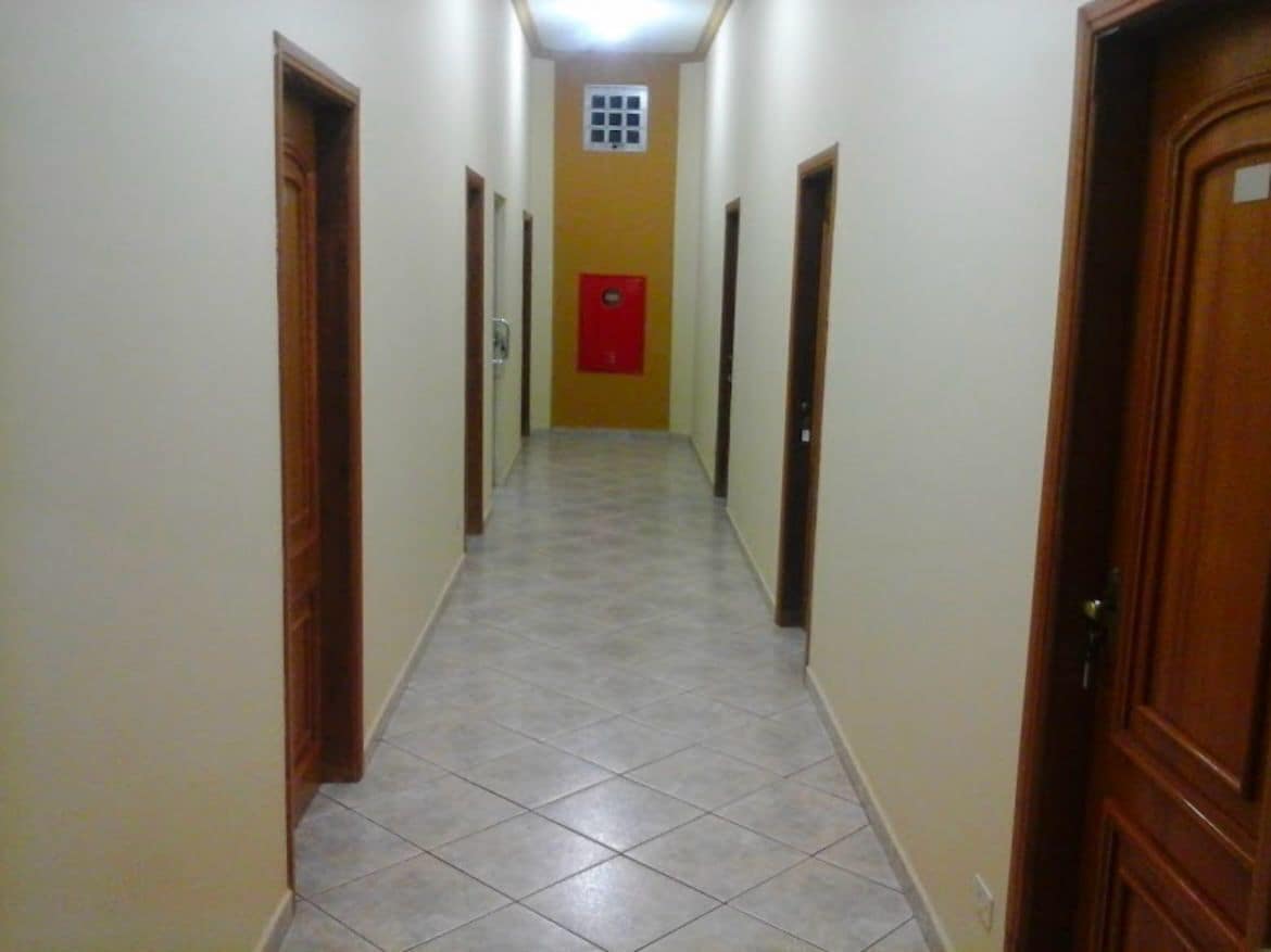 A narrow hallway with tiled flooring and wooden doors on both sides.