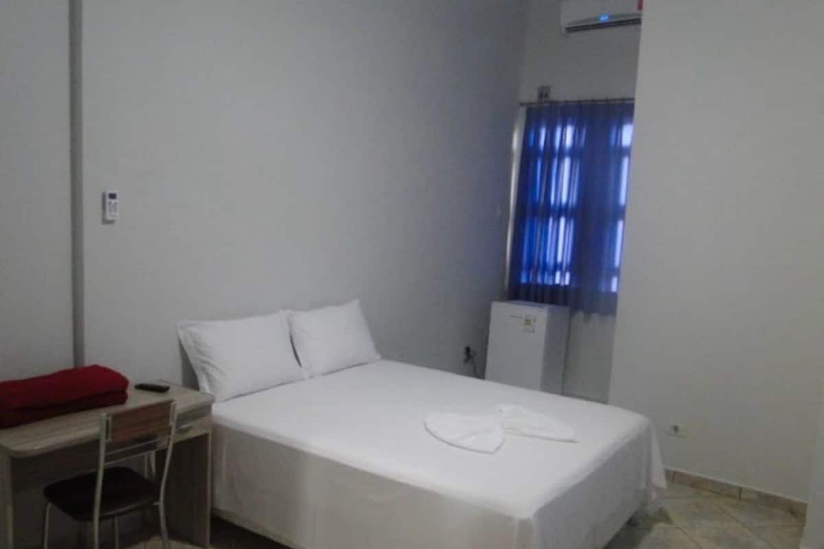 A small, clean room with a single bed, a desk, and a chair.