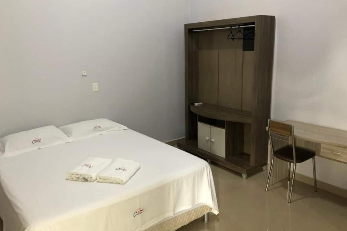 A hotel room with a bed, a wardrobe, a desk, and a chair.
