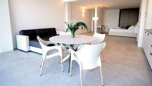 Una sala de estar moderna con una mesa redonda para comer, sillas blancas, un sofá negro y un jarrón decorativo.