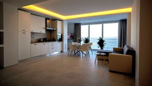Una cocina moderna con armarios blancos, una zona de comedor con mesa y sillas blancas, y un sofá.