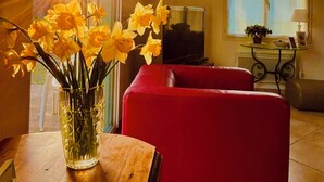 A living room with a red sofa, a wooden table with a vase of yellow flowers, and a television on a stand. - VILLA, INDOOR POOL, NEAR SAINT-ÉMILION/ BORDEAUX, IDEAL FOR FAMILY. (Puynormand)