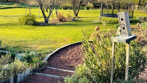 A park with a grassy area, trees, a swing set, and a wooden chair. - VILLA, INDOOR POOL, NEAR SAINT-ÉMILION/ BORDEAUX, IDEAL FOR FAMILY. (Puynormand)
