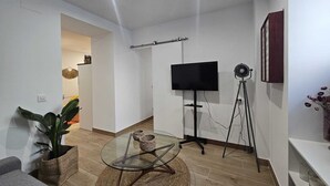 A modern living room with a glass coffee table, a flat-screen TV, a floor lamp, and a potted plant. - The Gabriels Chamberi (Madrid)