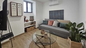 A modern living room with a grey sofa, a glass coffee table, and a large window. - The Gabriels Chamberi (Madrid)