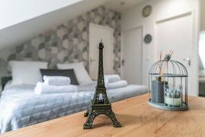 A model of the Eiffel Tower on a wooden table, a birdcage with a candle, and a bed with patterned bedding in the background.
