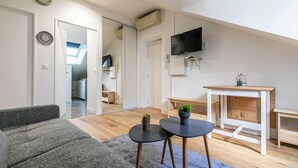 Ein modernes Wohnzimmer mit einer Couch, zwei kleinen Tischen, einem Fernseher und einem Holztisch mit einer Bank.