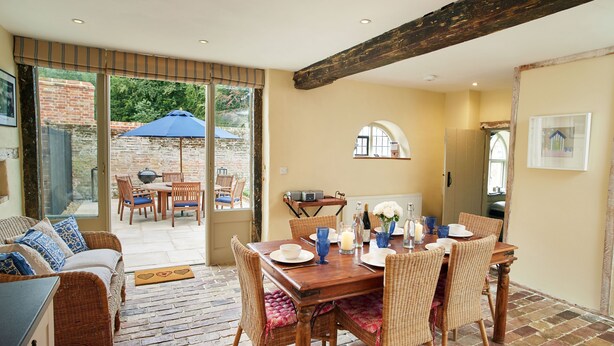 A dining area with a wooden table, wicker chairs, and a blue umbrella. - Stunning, dog friendly 3 bedroom/3 bathroom cottage close to beaches & short stroll to pub (Banningham)
