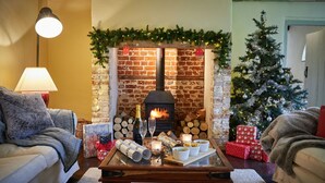 A cozy living room with a fireplace, a Christmas tree, and a coffee table with gifts and candles. - Stunning, dog friendly 3 bedroom/3 bathroom cottage close to beaches & short stroll to pub (Banningham)