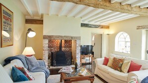 A cozy living room with a brick fireplace, white sofas, and a television. - Stunning, dog friendly 3 bedroom/3 bathroom cottage close to beaches & short stroll to pub (Banningham)