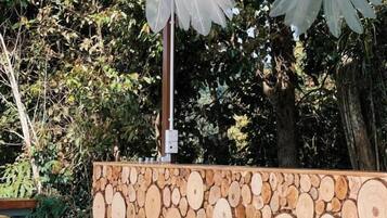 Un espace extérieur aménagé avec des chaises en osier et une table en bois, entouré d’un mur fait de rondins de bois empilés.