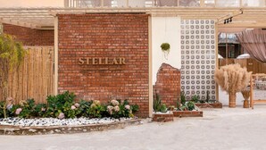 A hotel entrance with a brick facade, a sign reading "STELLAR", and a decorative wall with a lattice pattern.